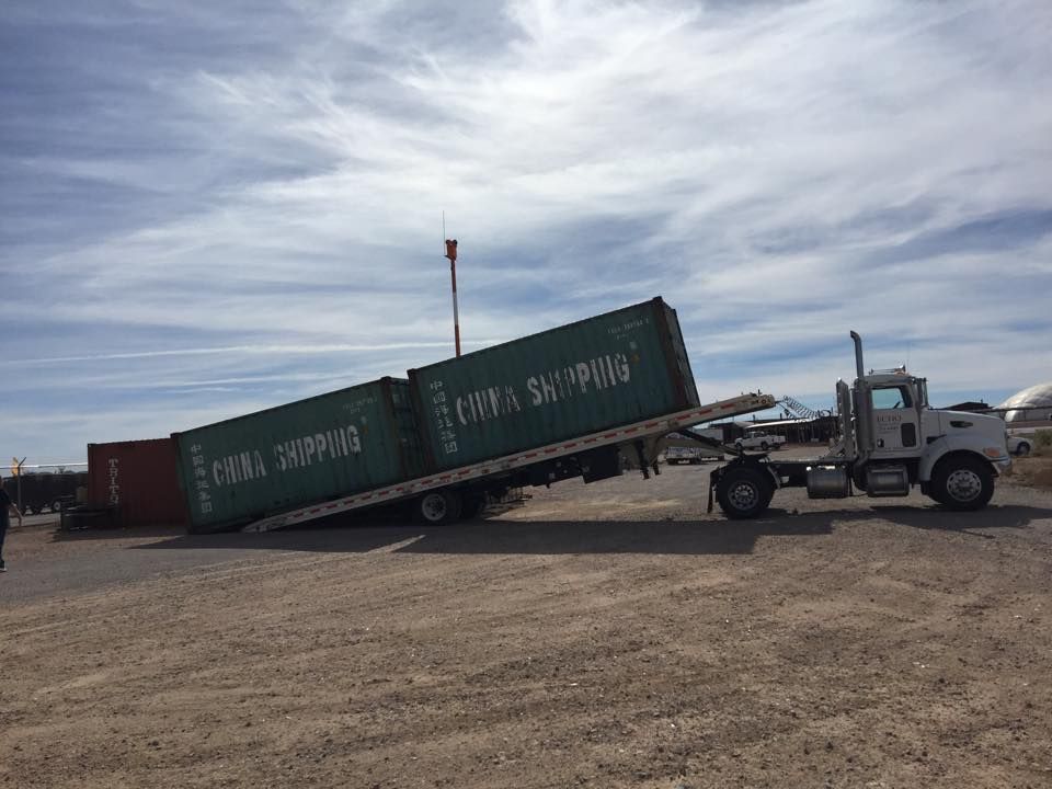 A semi truck is carrying a green shipping container on the back of it.