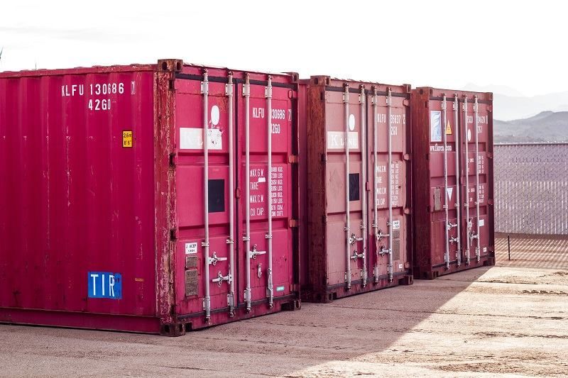 A row of red shipping containers are lined up in a parking lot.