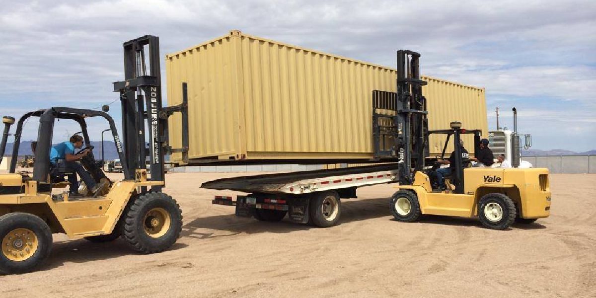 Two forklifts are carrying a container on a trailer.