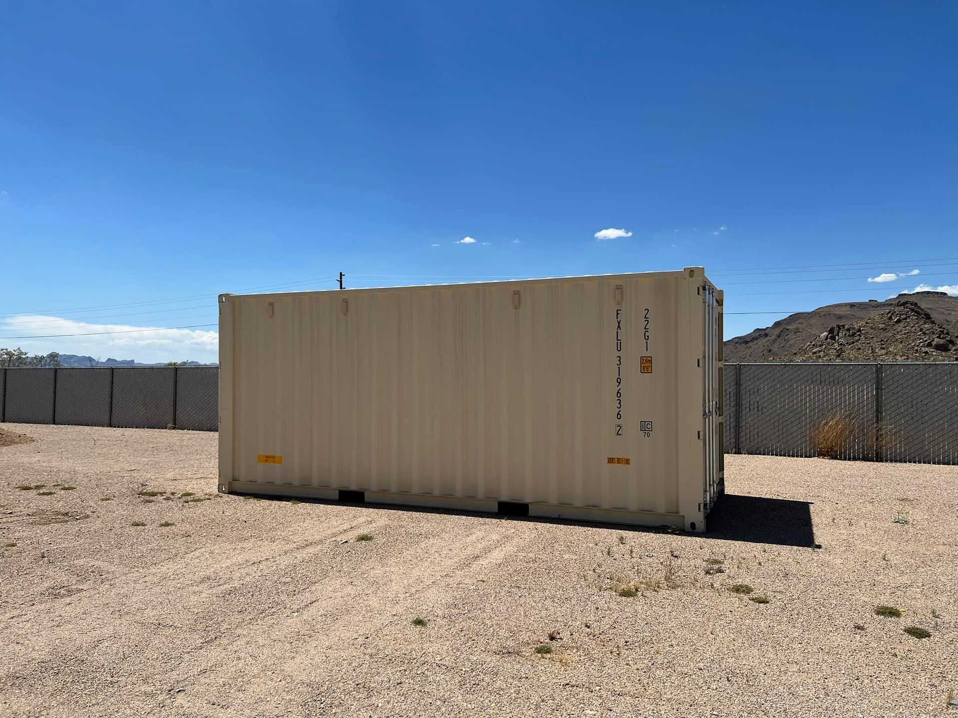A shipping container is sitting in the middle of a gravel field.