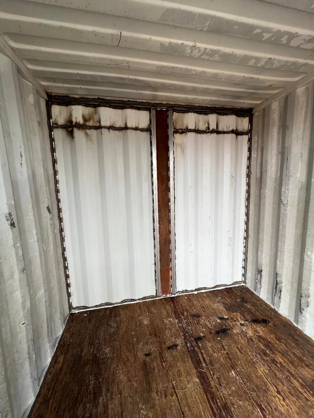 An empty shipping container with a wooden floor and white curtains.