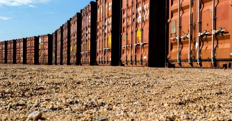 A row of shipping containers are lined up in a dirt field.