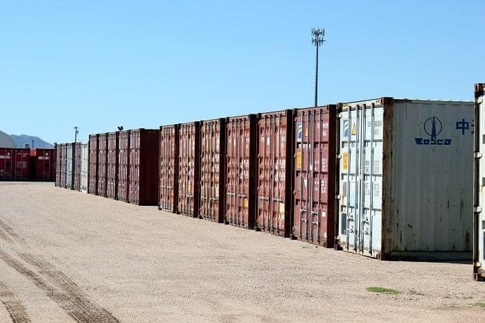 A row of shipping containers are lined up in a parking lot