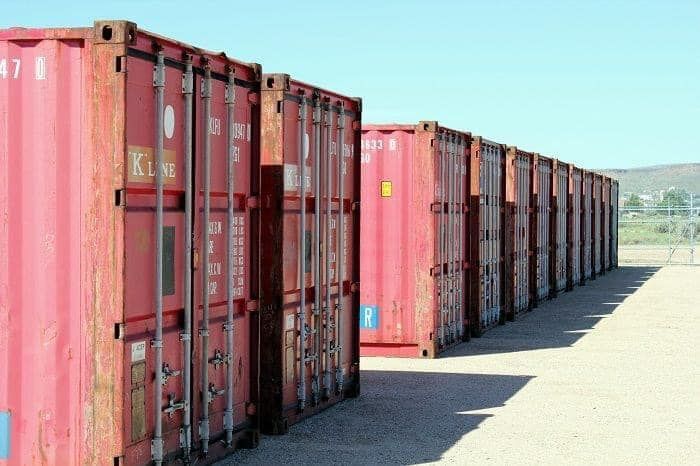 A row of red shipping containers are lined up in a parking lot.