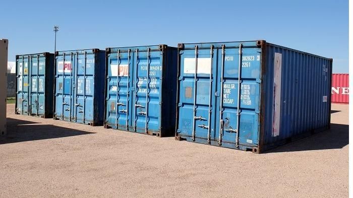 A row of blue shipping containers are lined up in a parking lot.