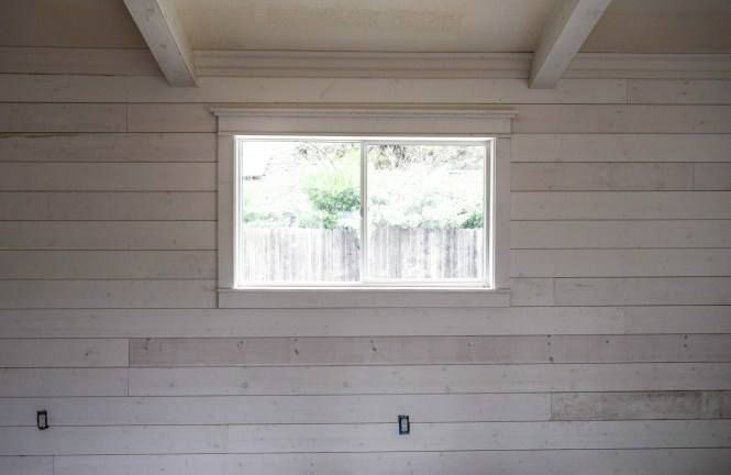 A white wall with a window in it and a fence in the background.