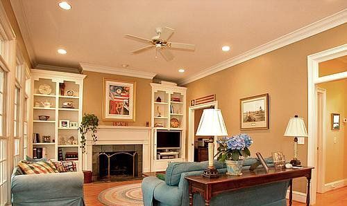 A living room with a couch , chair , table , fireplace and ceiling fan.