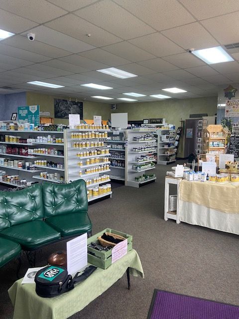 Interior of a pharmacy with shelves of products, green seating, and a display table.