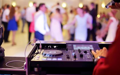 A dj is playing music at a party with a crowd of people dancing in the background.