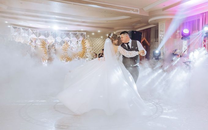 A bride and groom are dancing in the fog at their wedding reception.