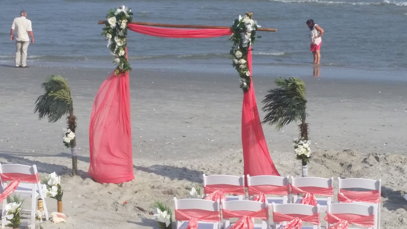 A wedding ceremony is set up on the beach with a red arch and white chairs.