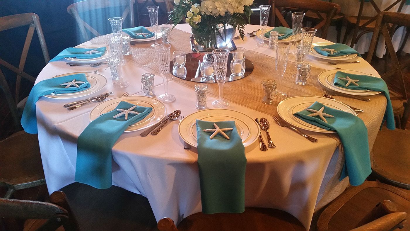 A round table is set for a wedding reception with blue napkins and plates.
