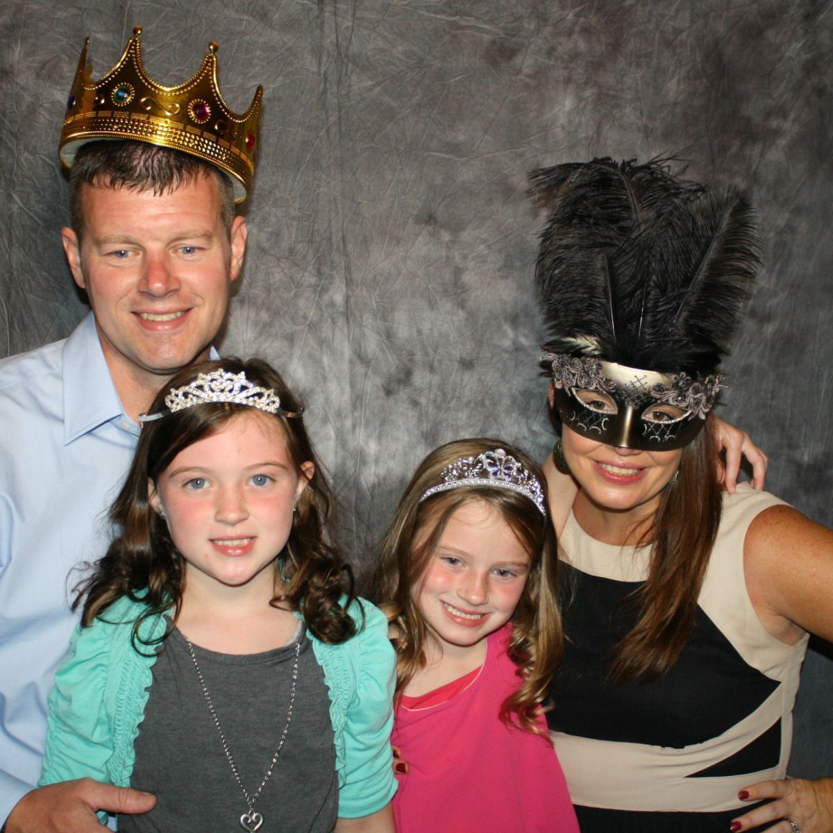 A man and two girls wearing crowns and masks pose for a picture