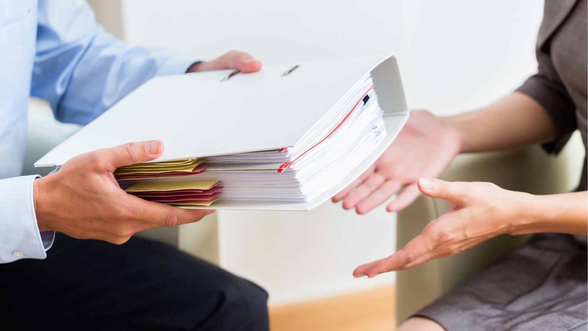 Two people exchange a thick stack of documents in a meeting room.