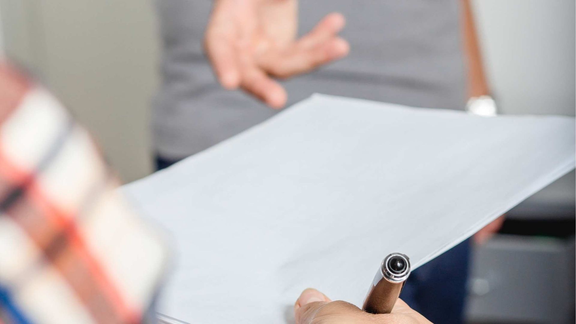 Hands holding a blank white sheet with a pen in the foreground during a meeting