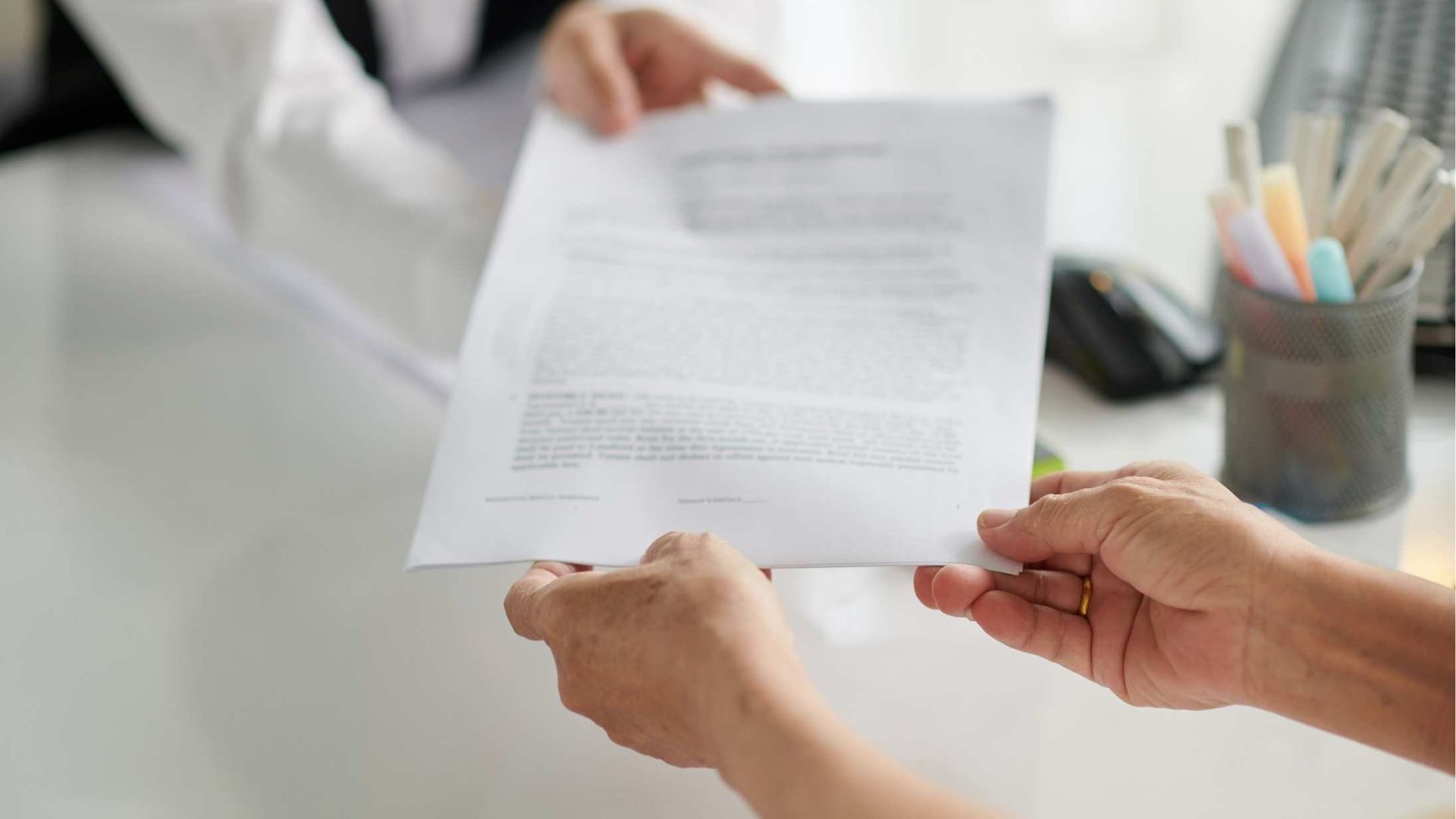 Hands reviewing a printed document at a desk, with a pen cup in the background.