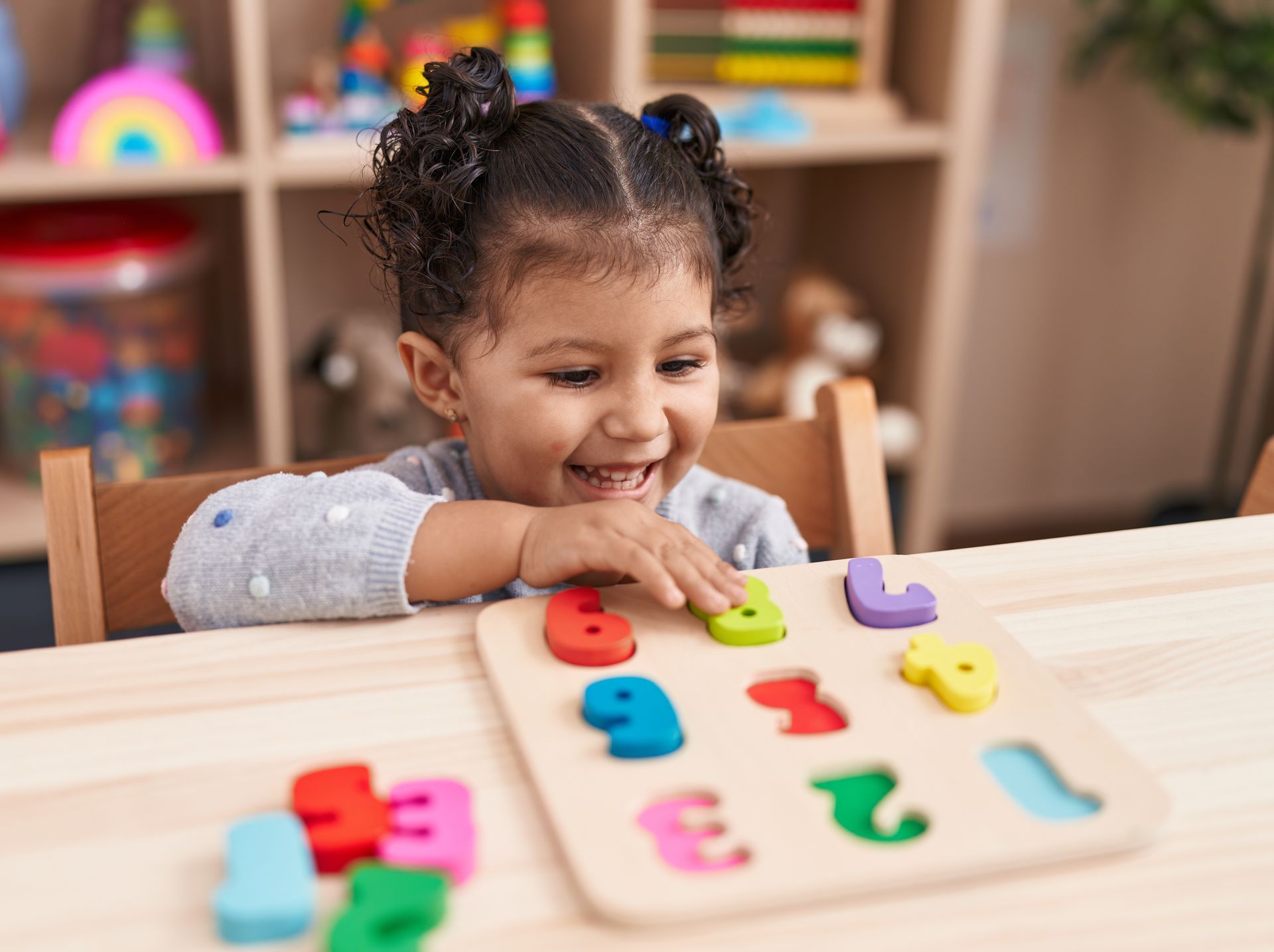 Child playing with colorful number puzzle, smiling. Indoors, wooden table.