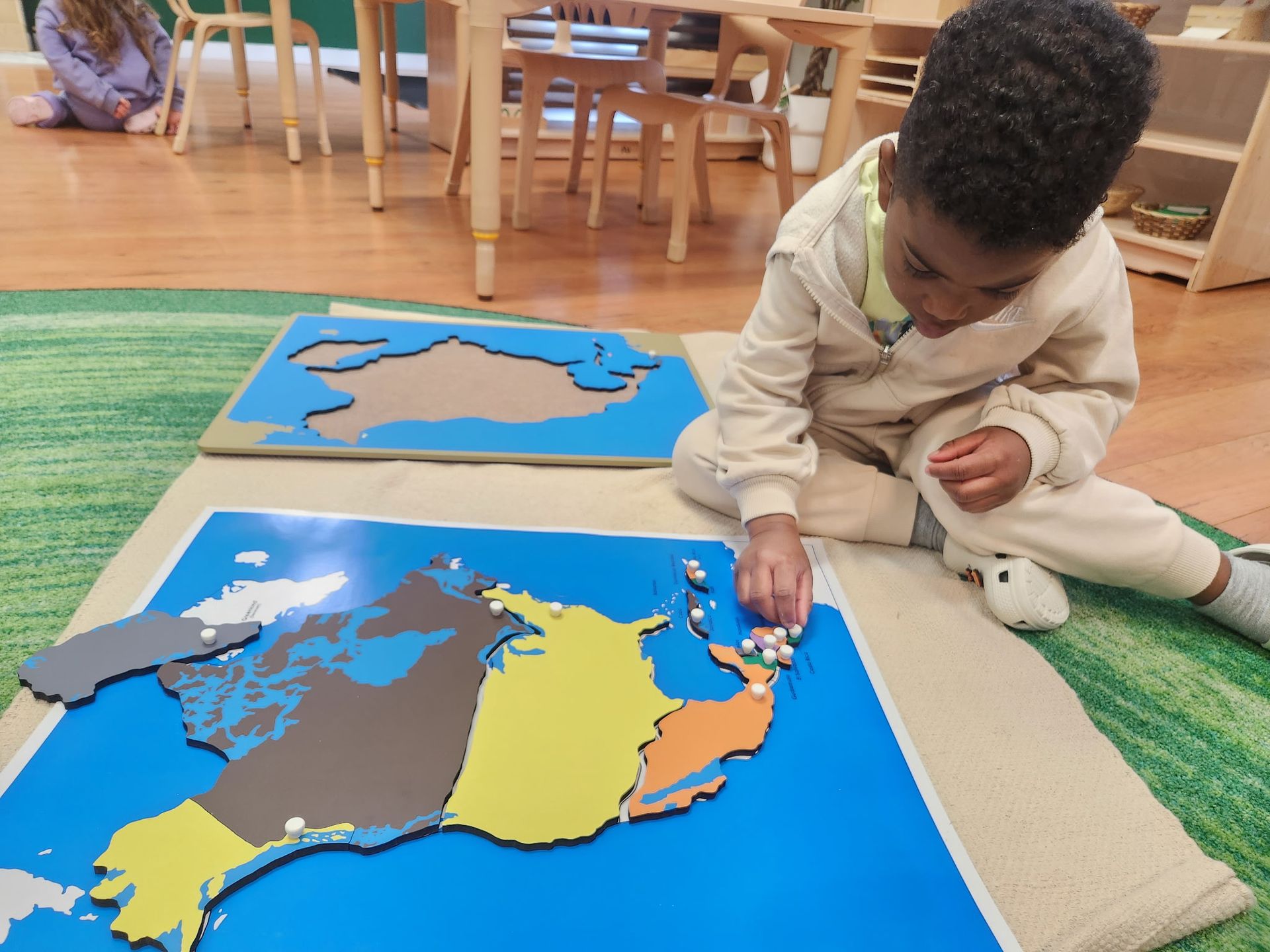 Boy placing pegs on a colorful puzzle map in a classroom setting.