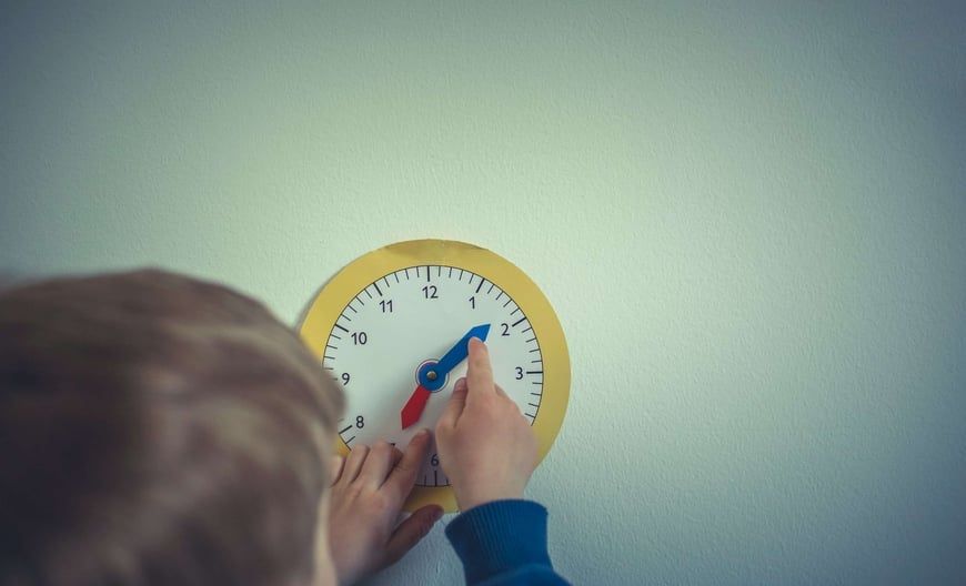 Child's hand pointing at a clock on a wall, adjusting the blue and red clock hands.