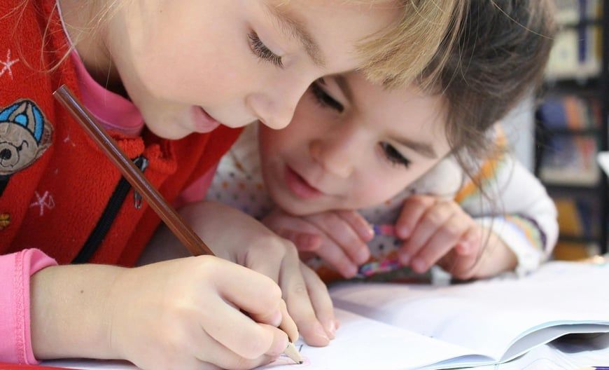 Two children closely studying a notebook, one writing with a pencil.