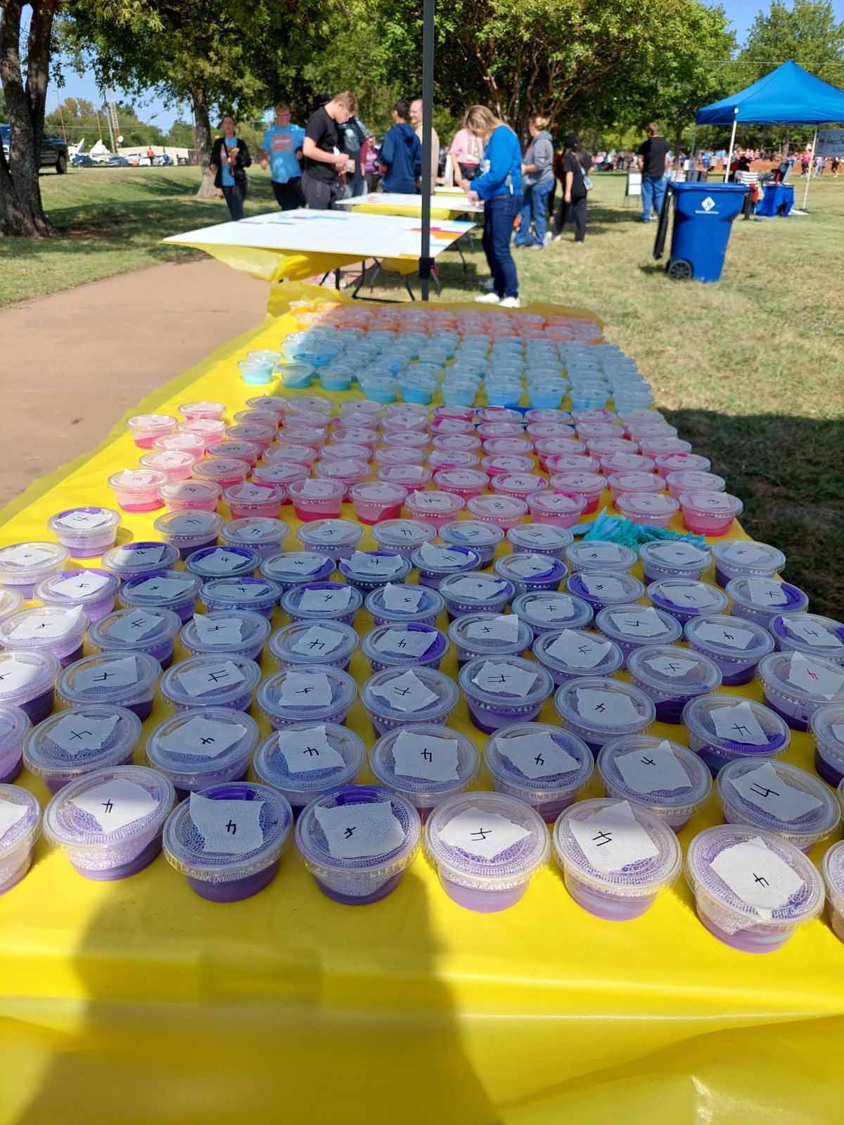 Rows of small cups with numbered labels, likely for an event, on a yellow table outdoors.