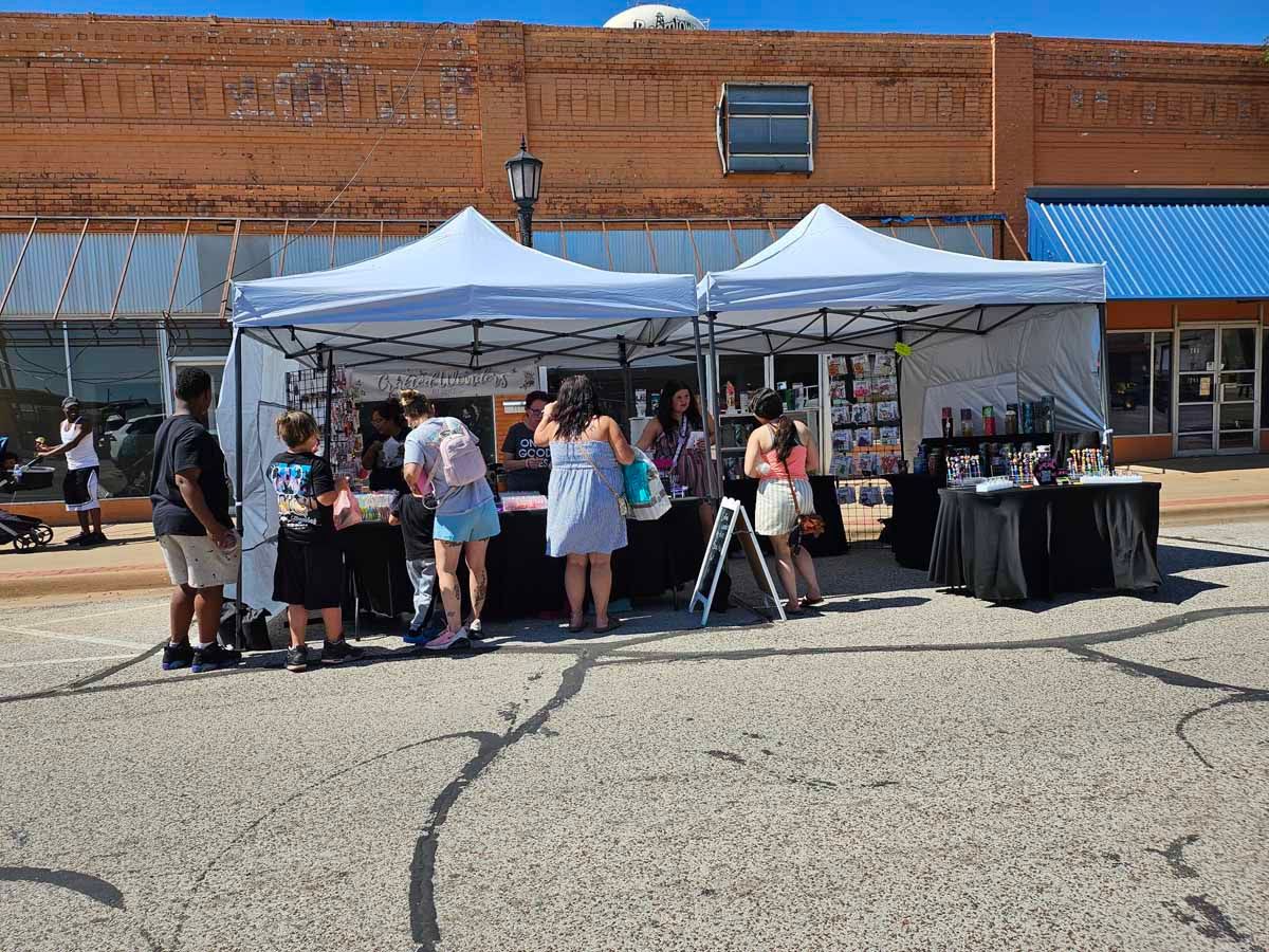 Outdoor vendor booths set up on a street; people browse and shop. Brick building background.