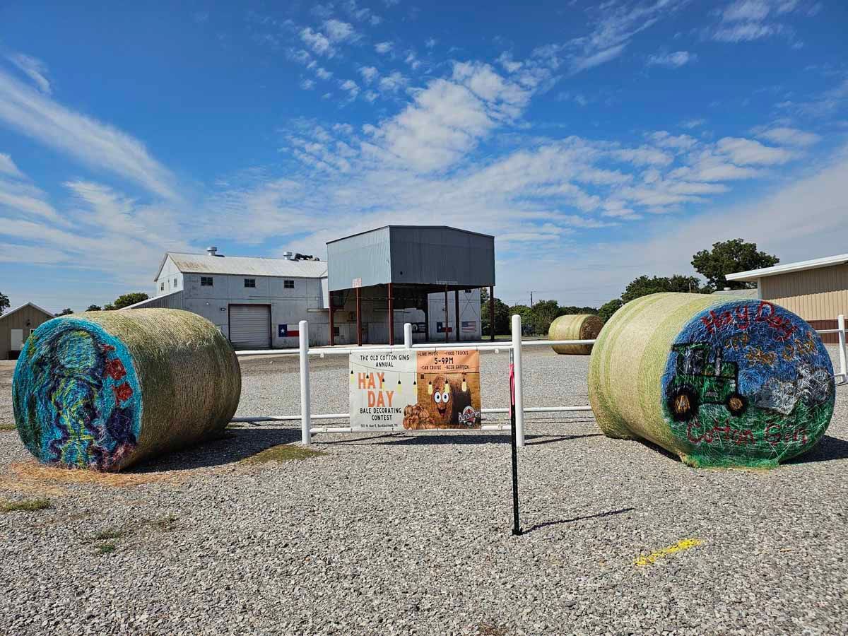 Two painted hay bales, an outdoor display, with industrial buildings in background, under blue sky.