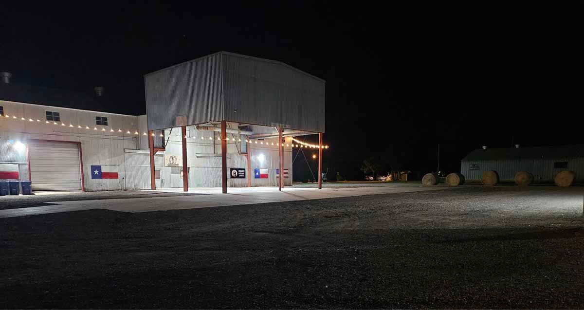 A large, lit-up building at night with the Texas flag painted on the side and surrounding open space.