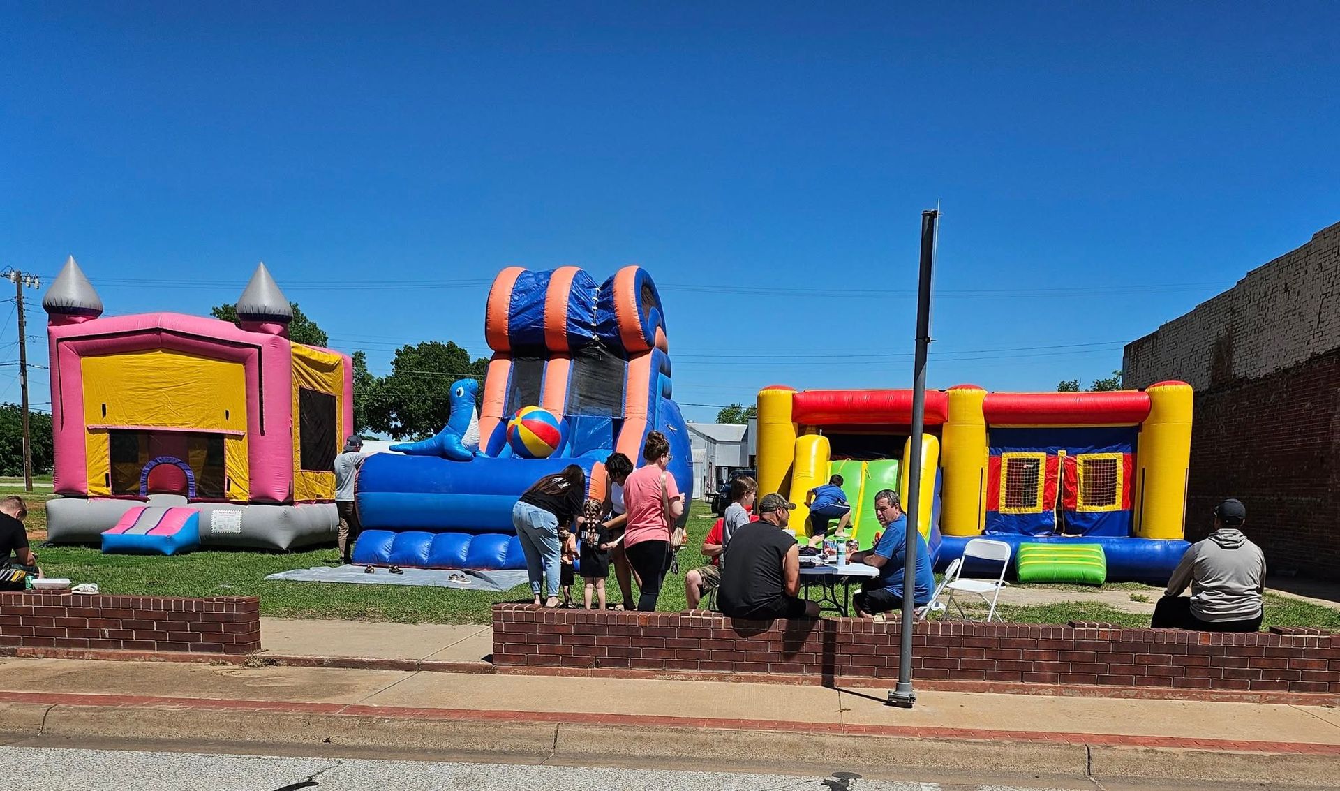 Bouncy castles set up outdoors; people gather nearby. Brightly colored inflatables on a sunny day.