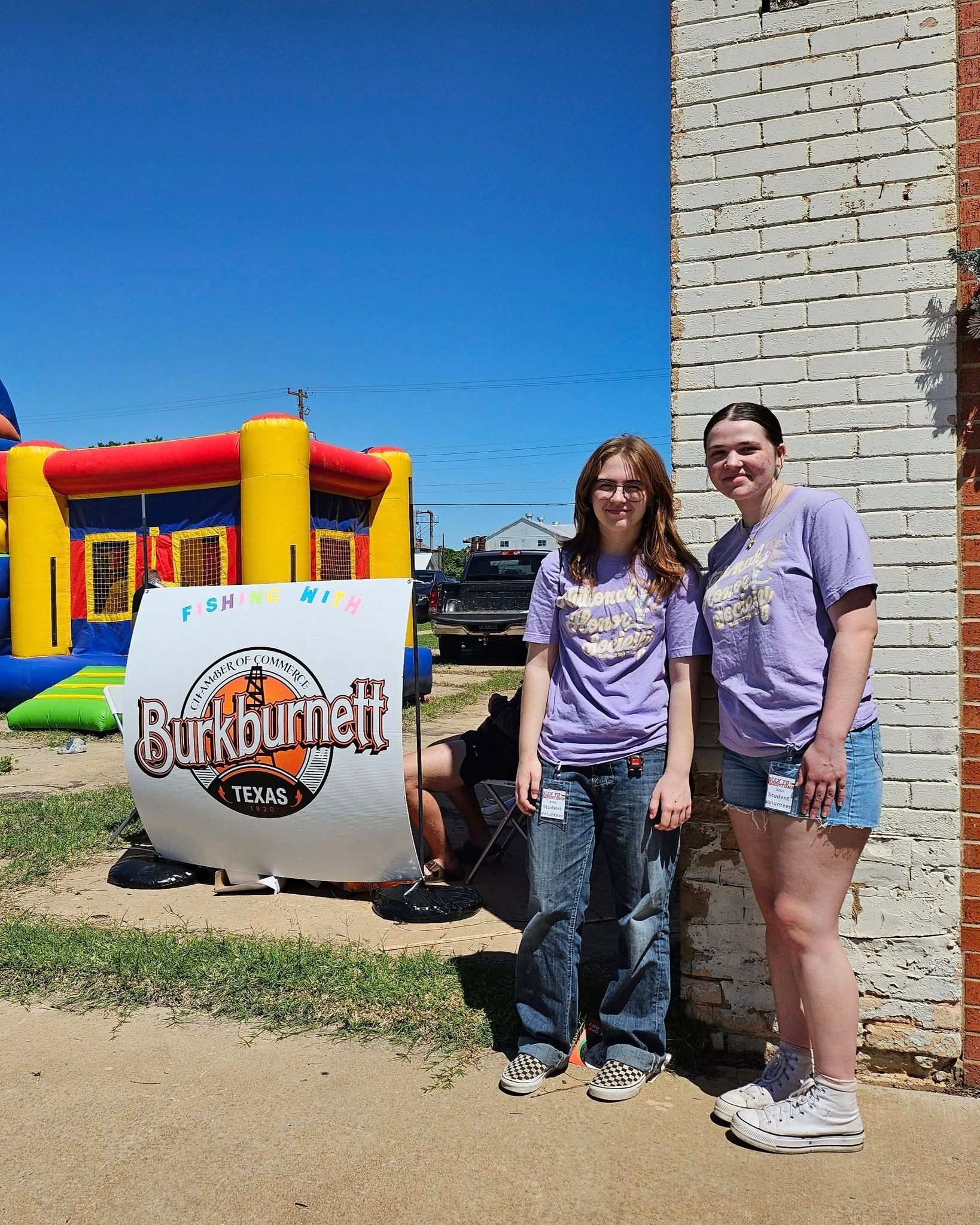Two people in purple shirts by a sign for 