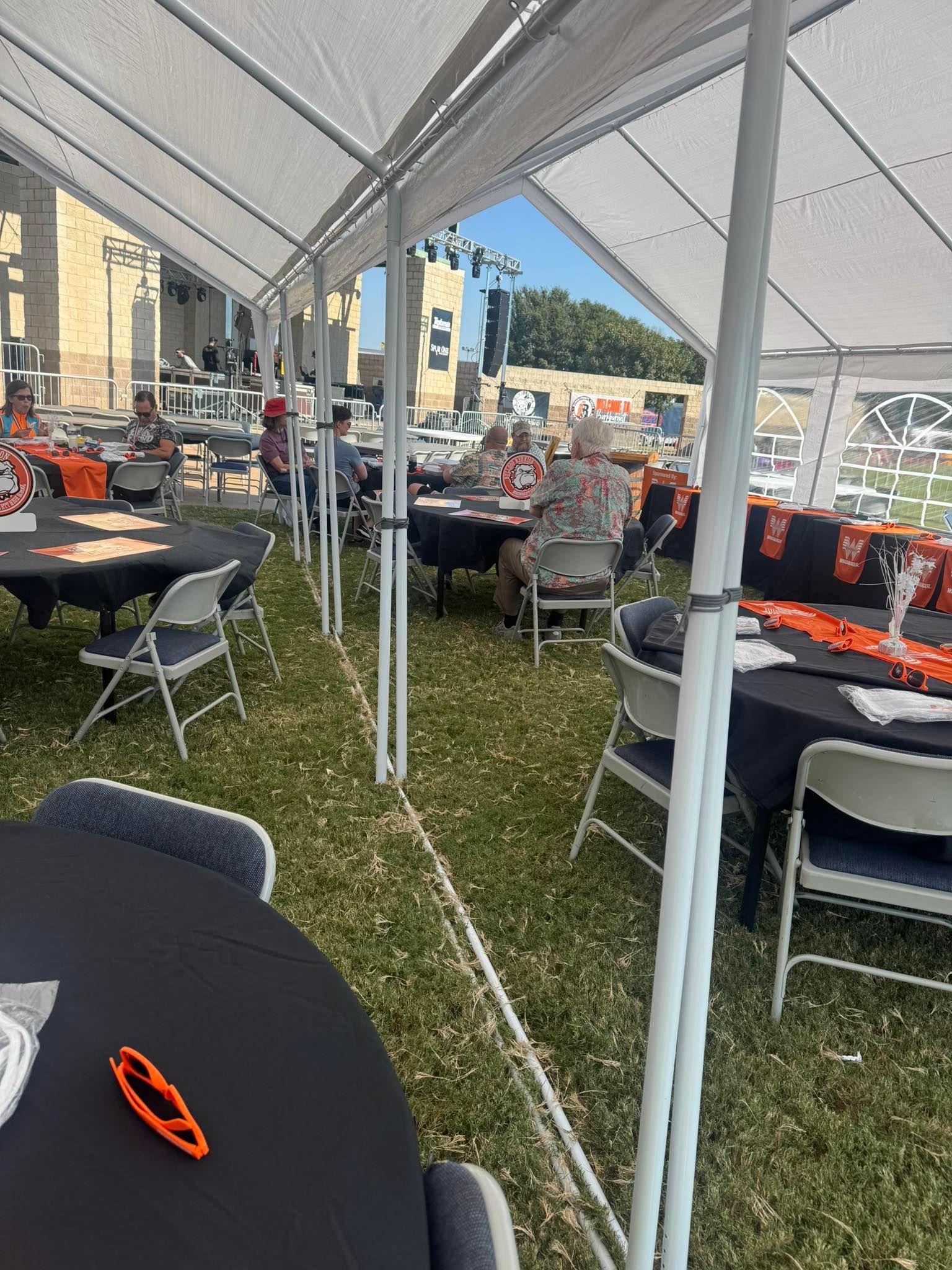 Outdoor event tent with black-covered tables, chairs, and decorations. Several people seated.