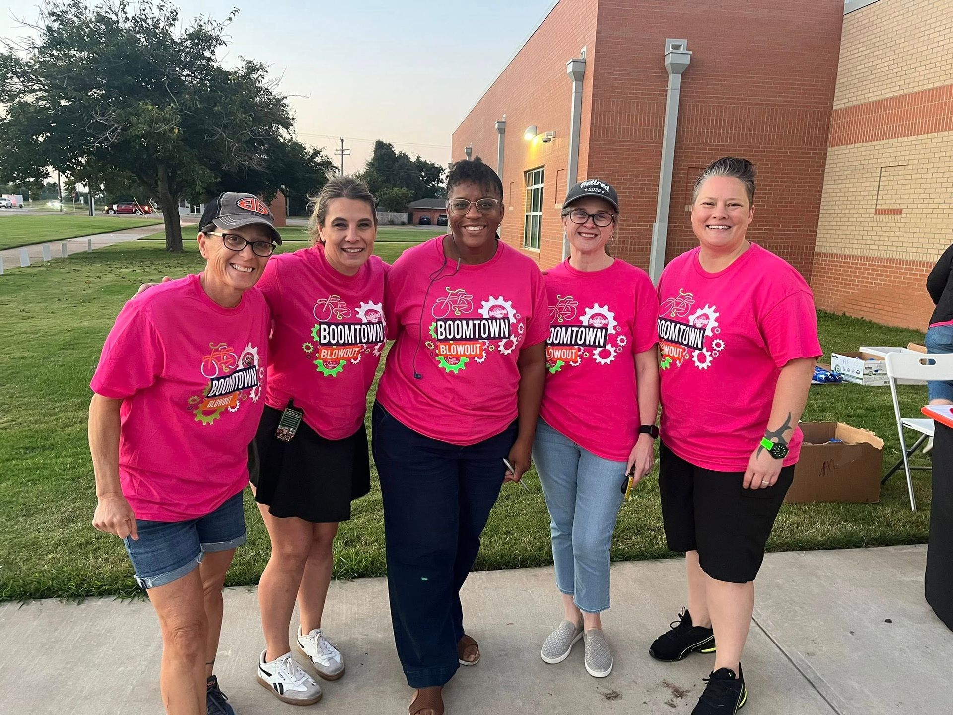 Five people in pink shirts smiling in front of a building.