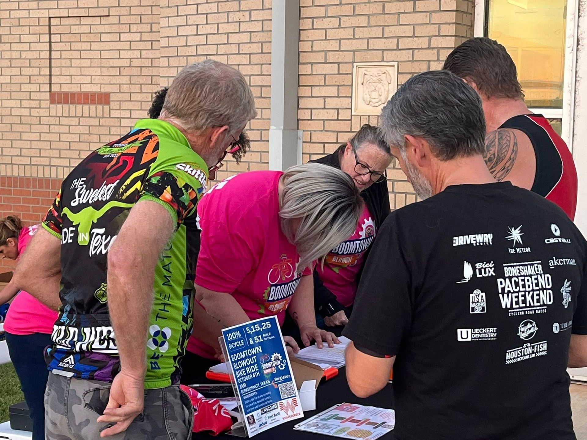 People register at a table outdoors. They are gathered around, looking at papers.