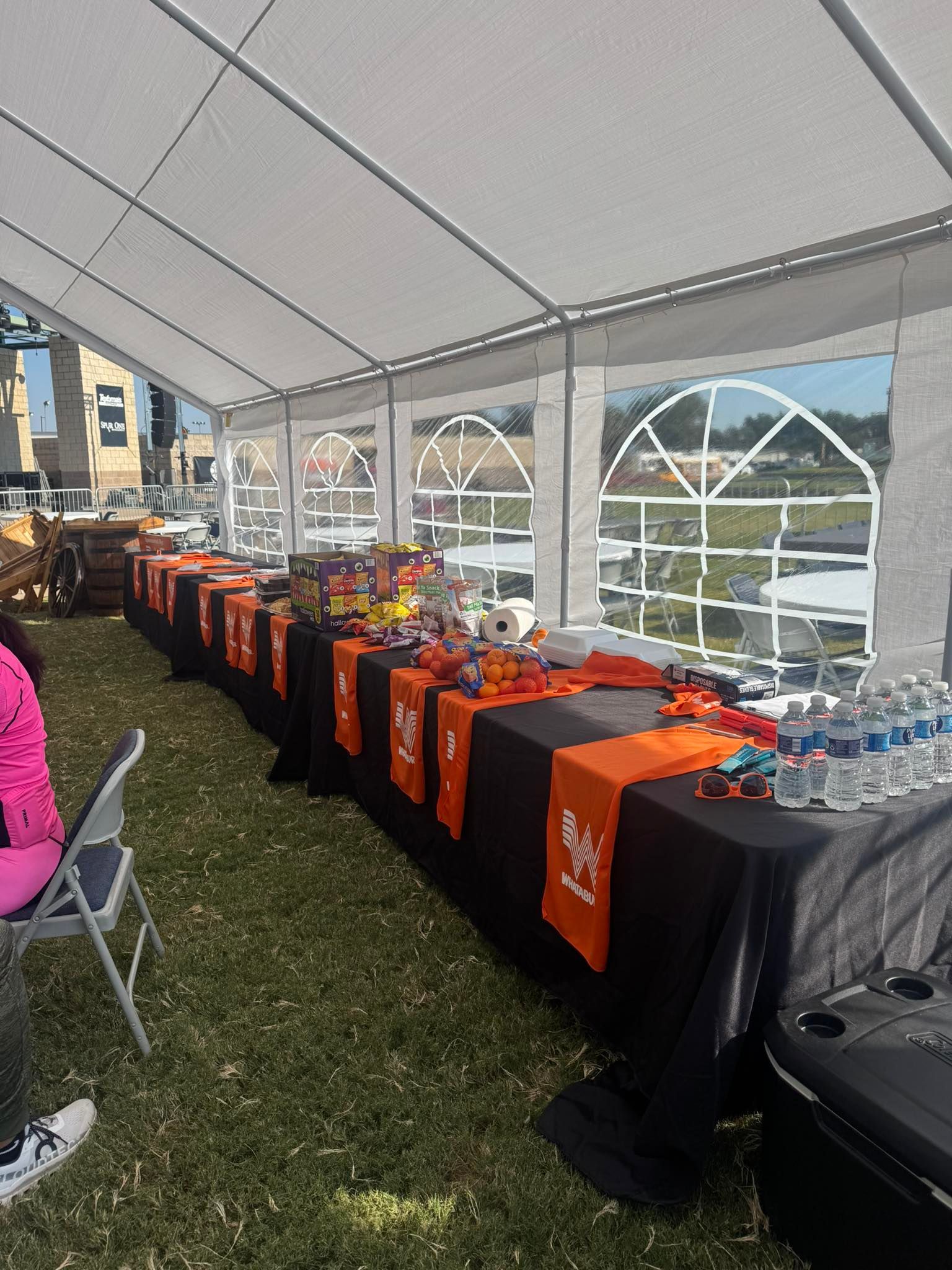 Long table under tent with orange and black decorations, various items displayed, water bottles.