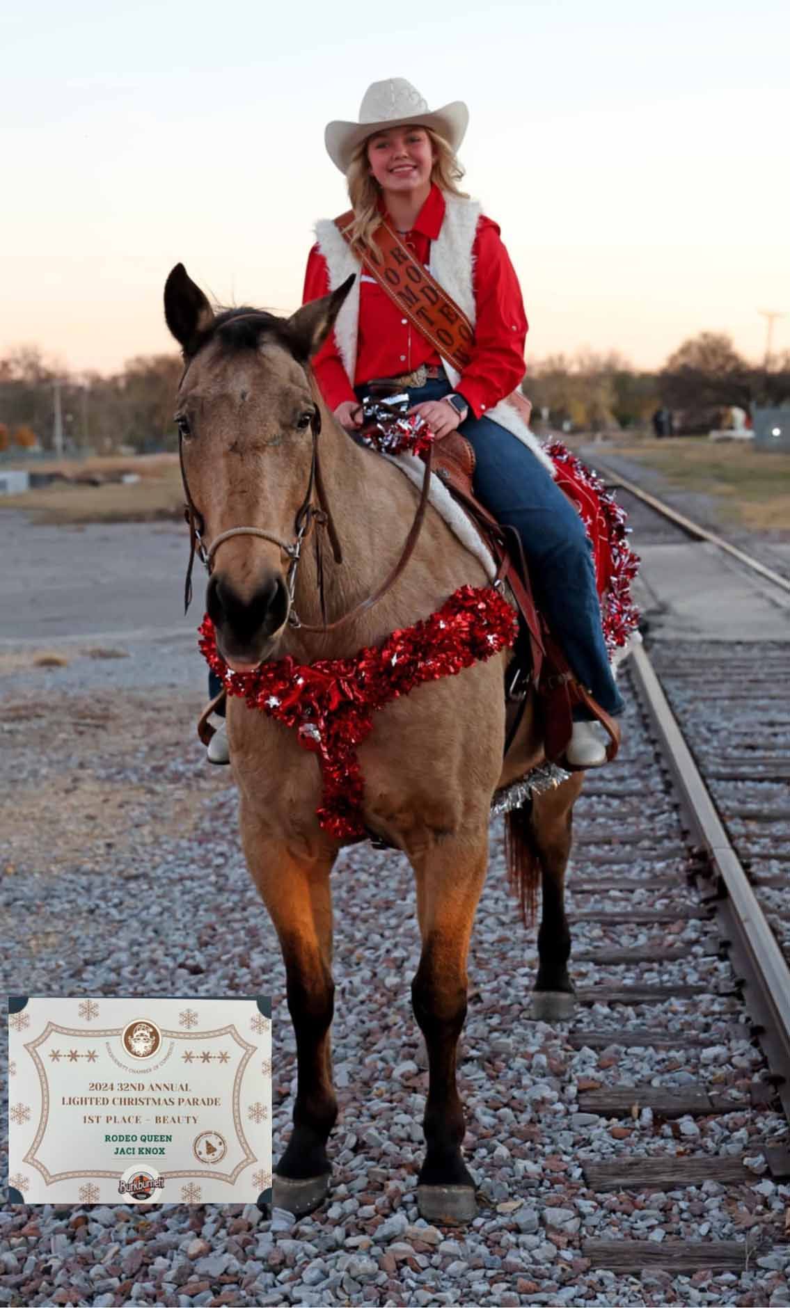 Woman in cowboy hat and sash on decorated horse at a train track.