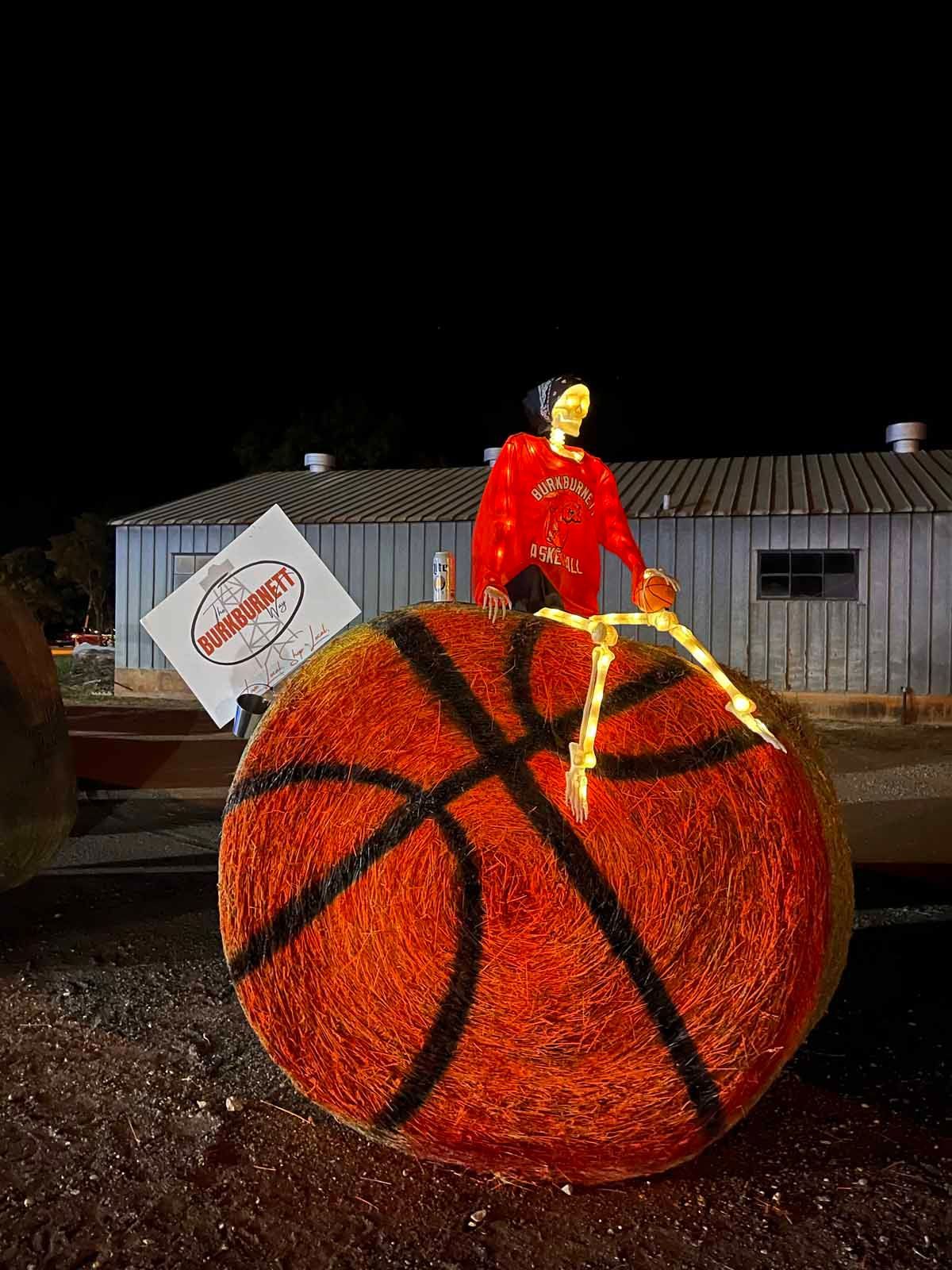 Large basketball decoration with person in red sweatshirt holding a sign. Nighttime scene.