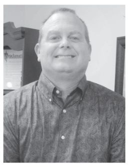 Smiling man in a button-down shirt. Office setting, focused on the upper body, neutral expression.