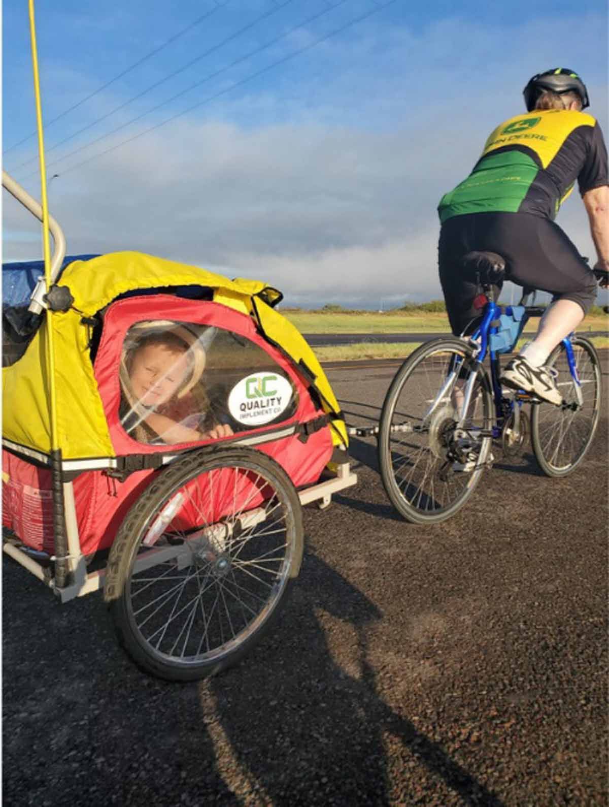 Person on a bike pulling a child in a red and yellow trailer.