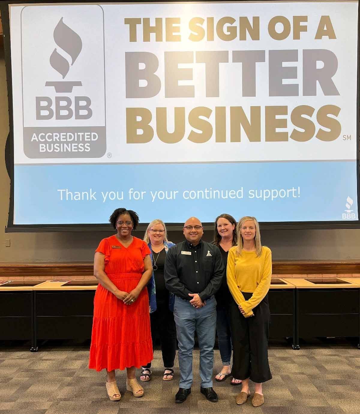 A group of five people standing in front of a screen displaying the BBB logo and text 
