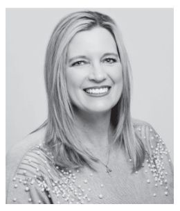 Woman with long blonde hair smiles, wearing a light sweater with embellished sleeves.