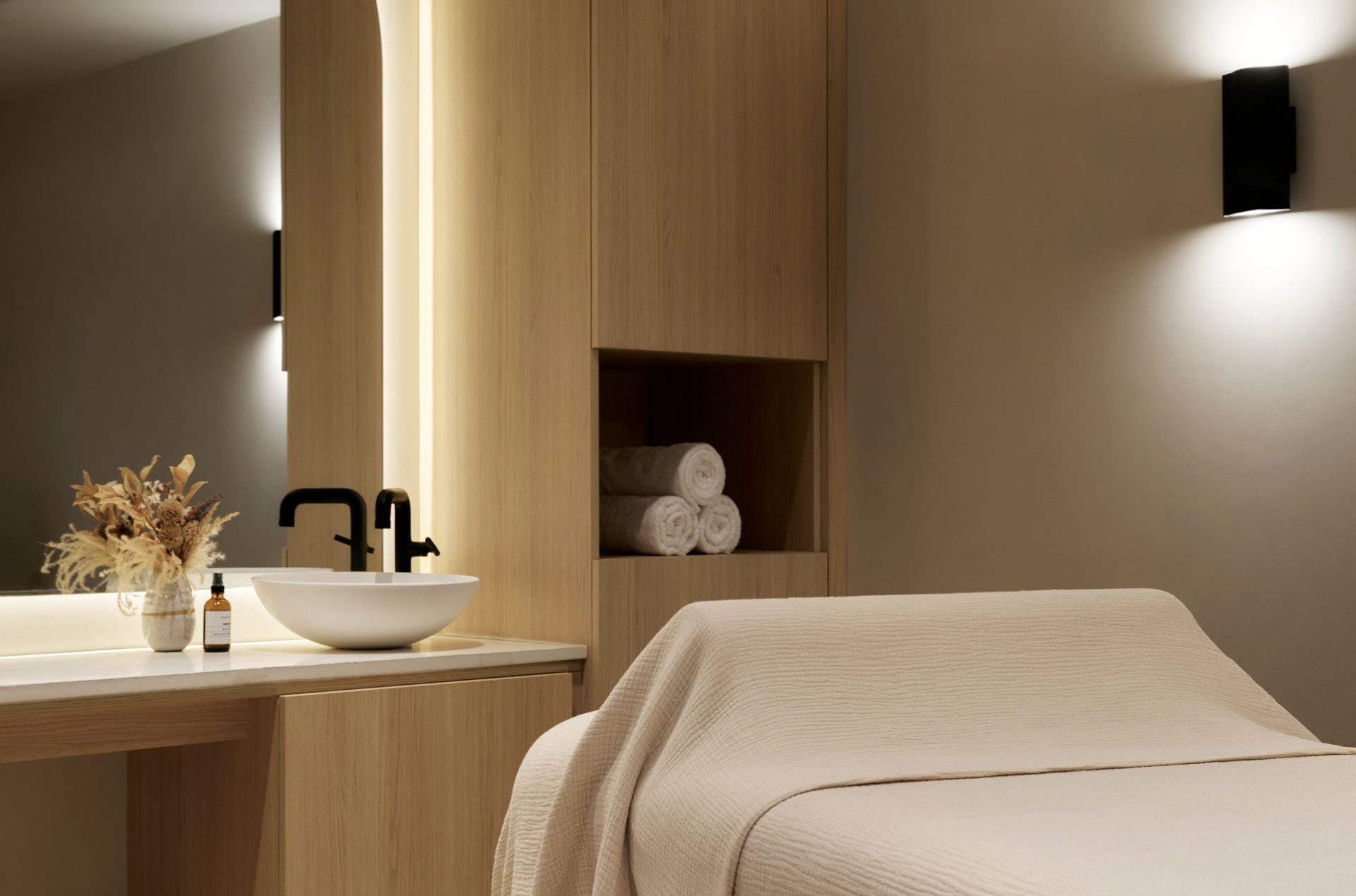 Spa room with massage table, sink, wooden cabinets, and wall sconces.