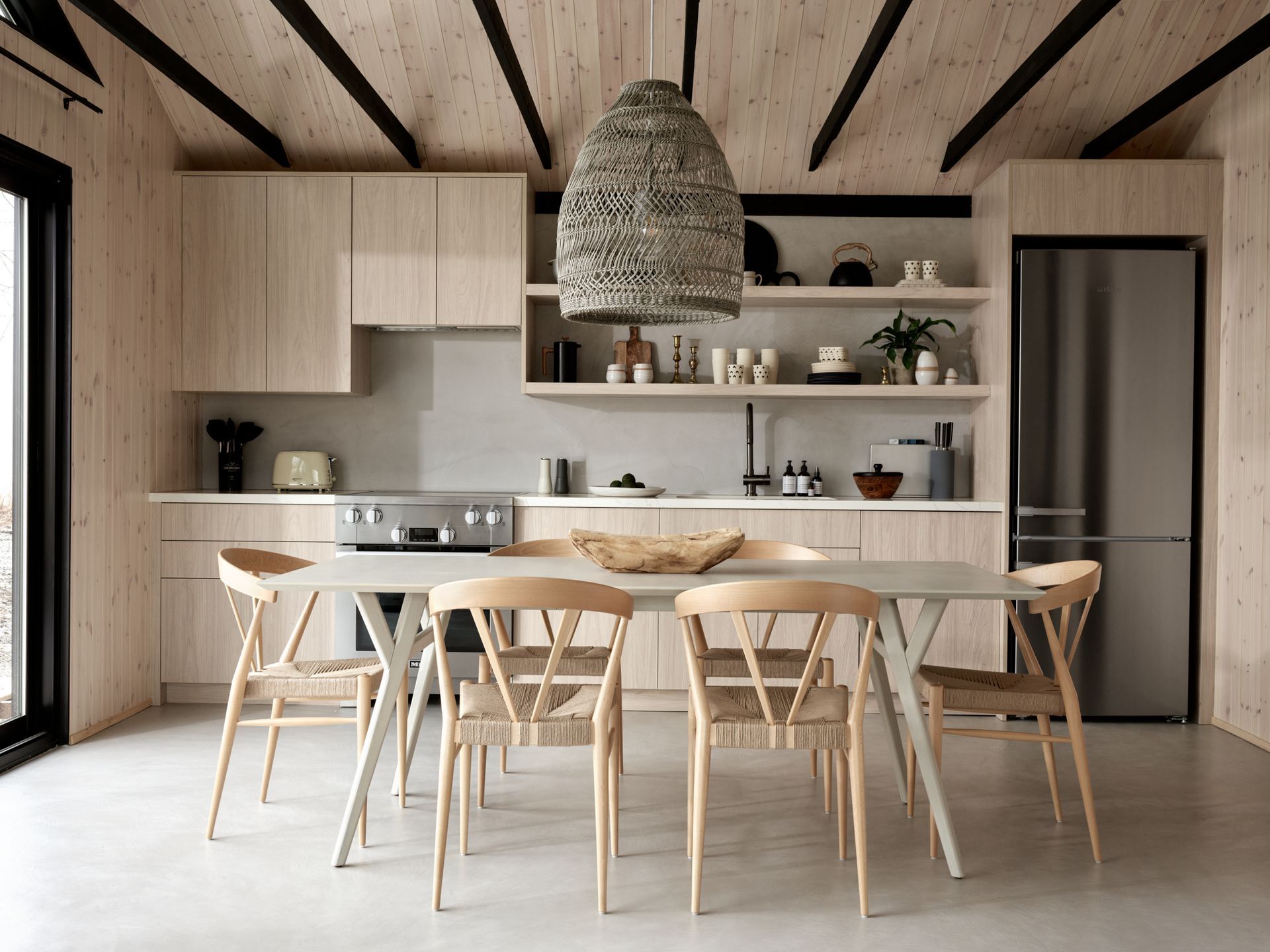 Modern kitchen with wooden cabinets, dining table, and woven pendant light.