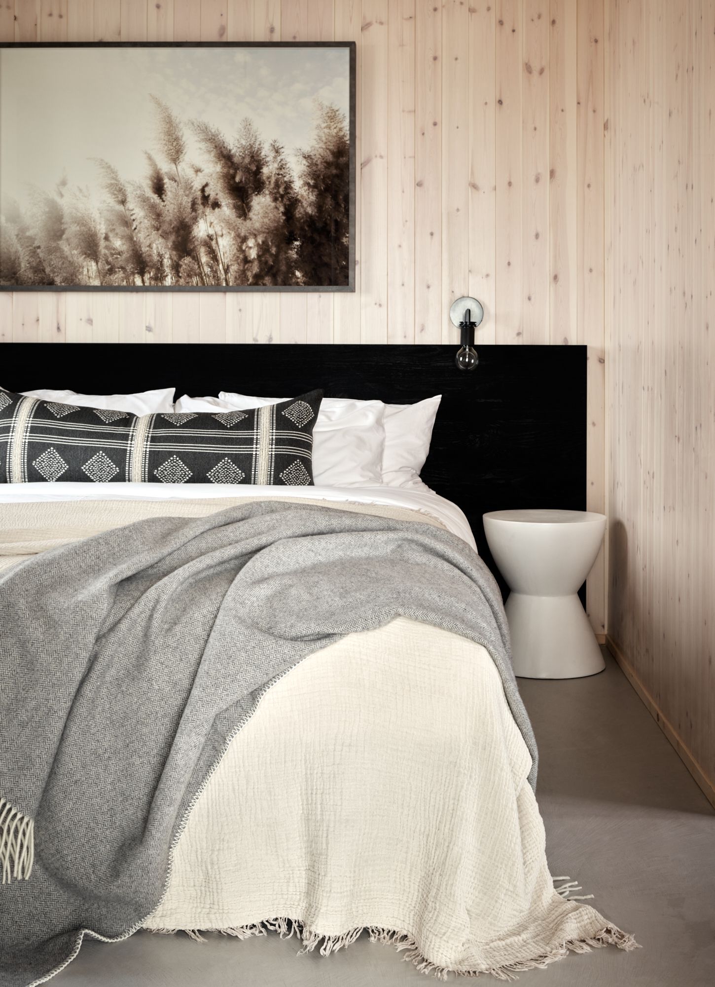 Bedroom with a black headboard, artwork, neutral bedding, gray throw, white side table, and wood-paneled walls.