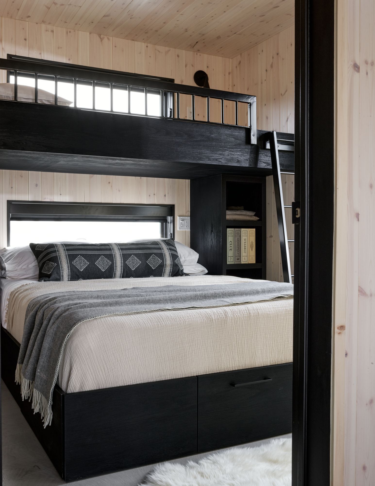 Bedroom with black bunk bed and storage, wood paneling, large window, and cozy bedding.