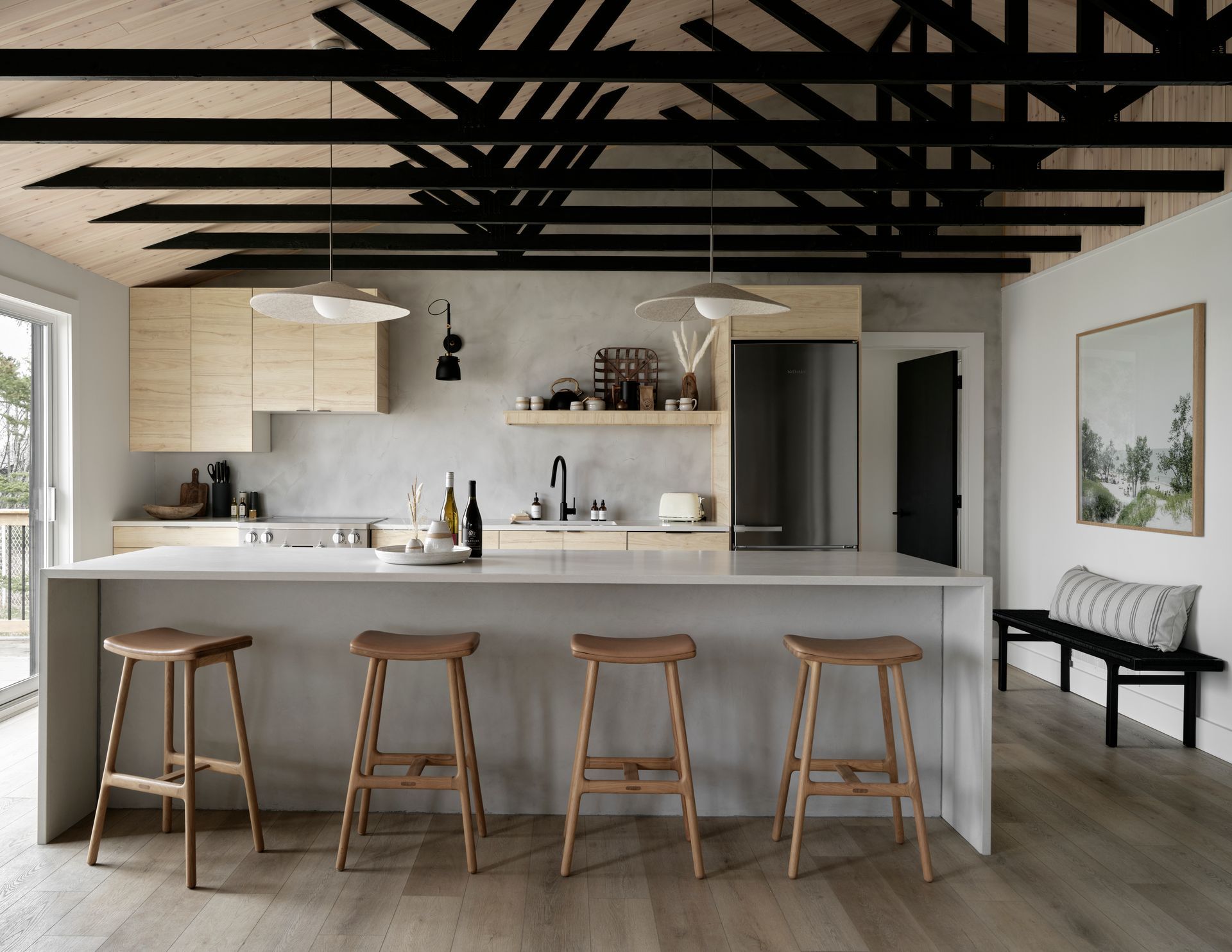 Modern kitchen with a large island, wooden stools, and exposed black beams on the ceiling.