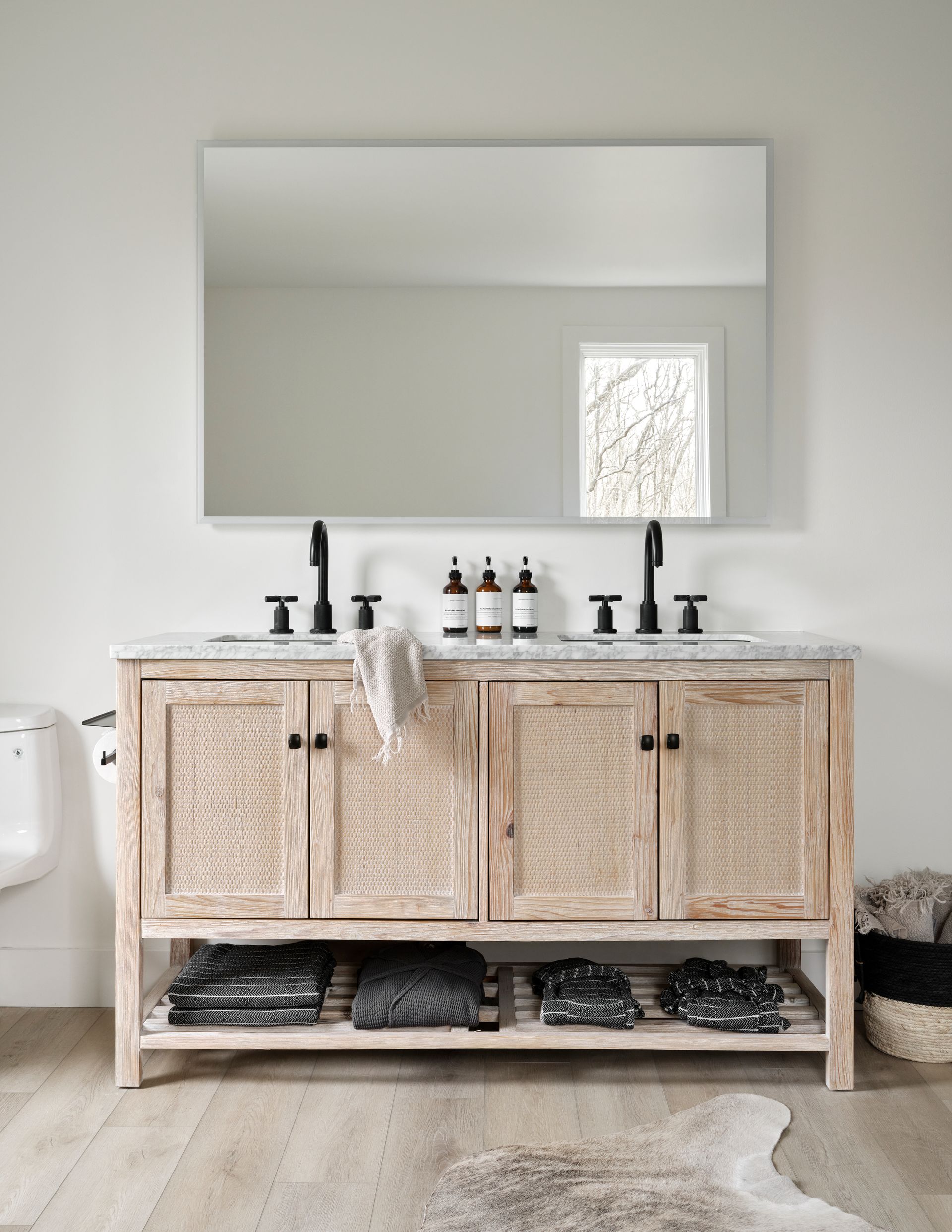 Bathroom with a light wooden double vanity, large mirror, black faucets, and woven cabinet doors.