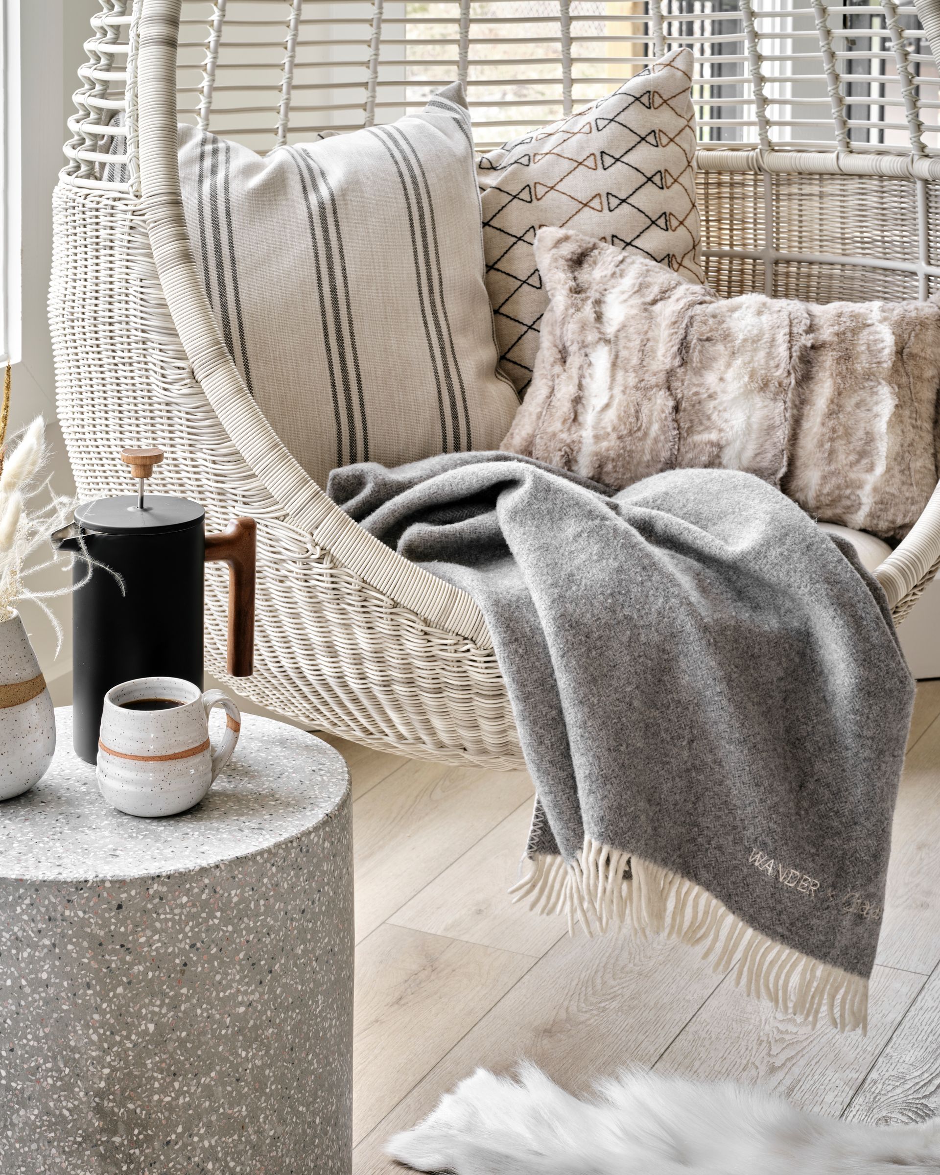 Cozy outdoor hanging chair with pillows and blanket; coffee on a side table.