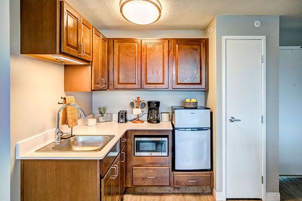 A small kitchen with wooden cabinets , stainless steel appliances , a sink , refrigerator and microwave.