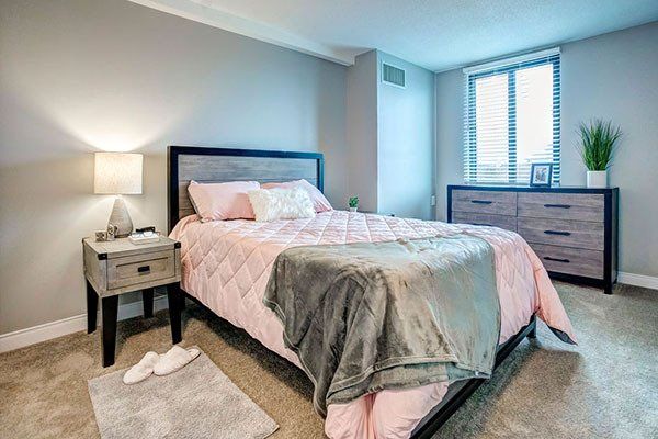 A bedroom with a bed , nightstand , dresser and window.