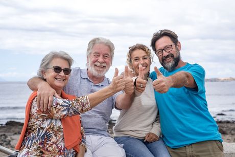 A group of people are sitting on a bench on the beach giving a thumbs up.